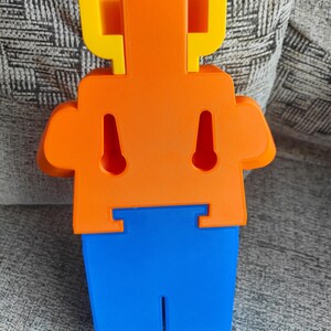 May include: A brightly colored, abstract 3D-printed figure in yellow, orange, and blue. The figure has a rectangular head, a torso with two keyhole-shaped cutouts, and a pair of arms. The lower portion is blue with a vertical slot. The text "OPPO Find X5" is at the bottom.