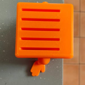 May include: Bright orange, square-shaped object with horizontal slots, and a small, rounded appendage. The object is resting on a gray surface. The image also includes the text "OPPO Find X5" and "HASSELBLAD".