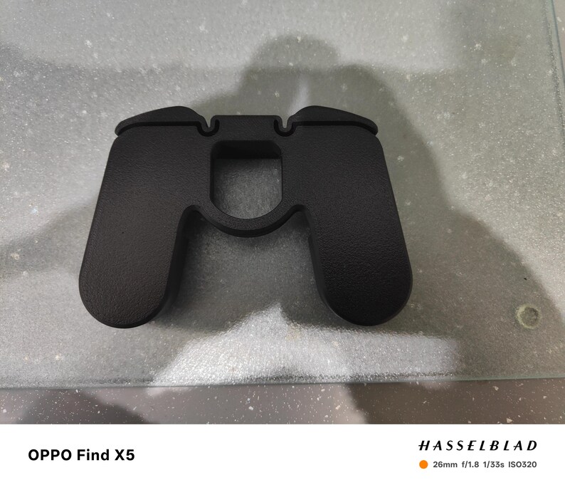 K&ouml;nnte beinhalten: Ein mattschwarzes Telefonzubeh&ouml;r in Form eines Gamecontrollers liegt auf einer hellgrauen Oberfl&auml;che. Das Zubeh&ouml;r hat eine strukturierte Oberfl&auml;che und einen mittigen Ausschnitt. Der Text "OPPO Find X5" ist unten links sichtbar.