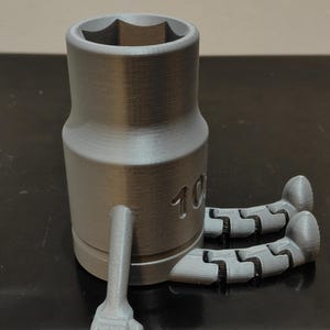 May include: A gray socket wrench with articulated arms and legs. The wrench has a hexagonal opening and the number "10" is visible on the side. The arms and legs are also gray and appear to be 3D printed.