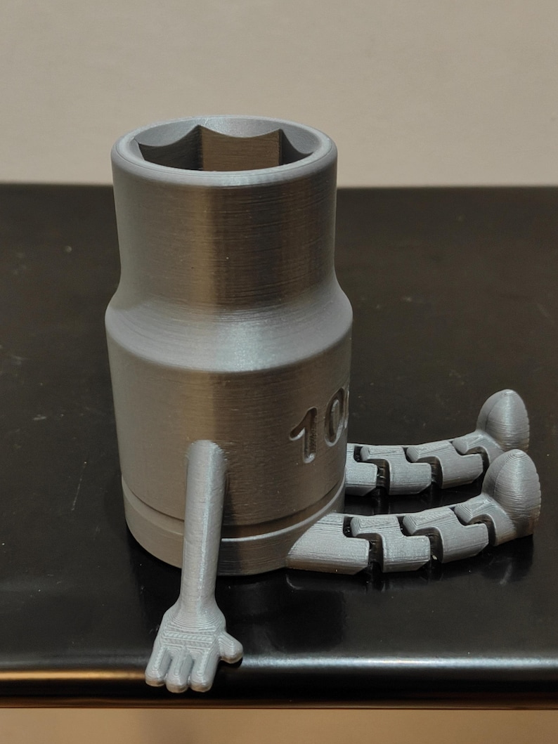 May include: A gray socket wrench with articulated arms and legs. The wrench has a hexagonal opening and the number "10" is visible on the side. The arms and legs are also gray and appear to be 3D printed.