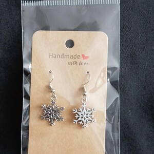 May include: A pair of silver snowflake earrings on a brown card with the text "Handmade with love" in a clear plastic bag. The earrings have a detailed snowflake design and a silver hook.