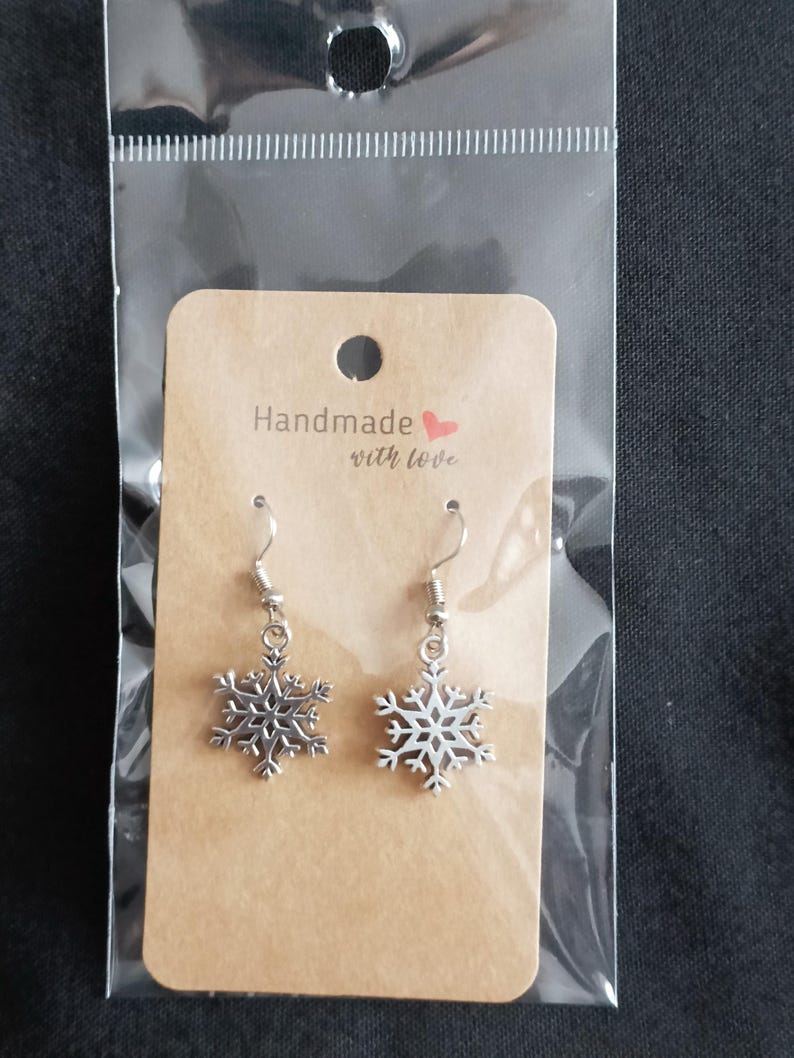 May include: A pair of silver snowflake earrings on a brown card with the text "Handmade with love" in a clear plastic bag. The earrings have a detailed snowflake design and a silver hook.
