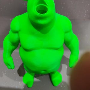 K&ouml;nnte beinhalten: Hellgr&uuml;ne Figur eines Cartoon-Ogers mit offenem Mund. Die Figur hat gro&szlig;e Arme und Ohren und steht auf einer grauen Oberfl&auml;che. Das Bild wurde mit einer OPPO Find X5 Kamera aufgenommen.
