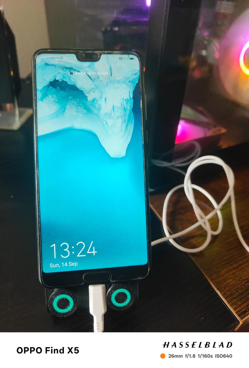 K&ouml;nnte beinhalten: Ein Smartphone mit einem hellblauen Bildschirm, der die Uhrzeit 13:24 und das Datum, Sonntag, 14. September, anzeigt. Das Telefon befindet sich in einem schwarzen St&auml;nder mit gr&uuml;nen Akzenten und einem wei&szlig;en Ladekabel. Das Telefonmodell ist OPPO Find X5.