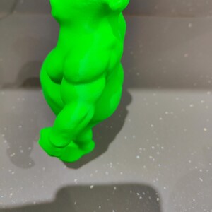 K&ouml;nnte beinhalten: Eine leuchtend gr&uuml;ne Skulptur eines menschlichen Torsos mit definierter Muskulatur. Die Figur ist in einer dynamischen, verdrehten Position dargestellt. Die Skulptur steht vor einem neutralen, gesprenkelten Hintergrund.