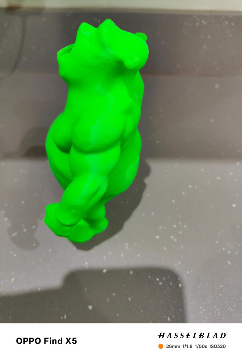 K&ouml;nnte beinhalten: Eine leuchtend gr&uuml;ne Skulptur eines menschlichen Torsos mit definierter Muskulatur. Die Figur ist in einer dynamischen, verdrehten Position dargestellt. Die Skulptur steht vor einem neutralen, gesprenkelten Hintergrund.