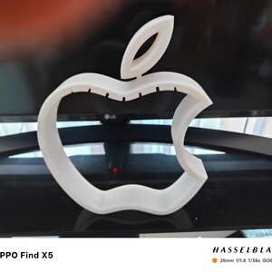 May include: A white, three-dimensional Apple logo, with the iconic bite taken out of the right side. The logo is set against a blurred background. The text "OPPO Find X5" is at the bottom left, and "HASSELBLAD" is at the bottom right.