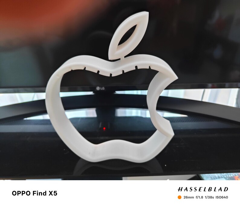 May include: A white, three-dimensional Apple logo, with the iconic bite taken out of the right side. The logo is set against a blurred background. The text "OPPO Find X5" is at the bottom left, and "HASSELBLAD" is at the bottom right.