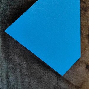 May include: A bright blue, geometric-shaped object with a textured surface. The object is set against a dark, textured background. The shape is a modified triangle, with one side longer than the others.
