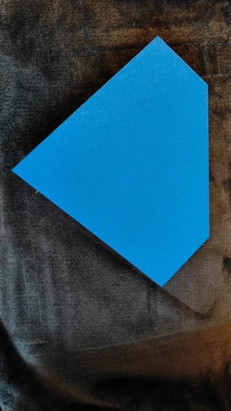 May include: A bright blue, geometric-shaped object with a textured surface. The object is set against a dark, textured background. The shape is a modified triangle, with one side longer than the others.