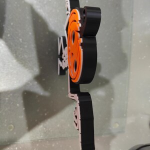 May include: A black, white, and orange film reel logo. The logo is made of layered materials and is mounted on a clear surface. The logo is a stylized representation of a film reel, with the word "film" incorporated into the design.
