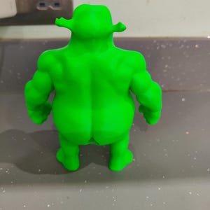 K&ouml;nnte beinhalten: Hellgr&uuml;ne Figur einer Figur mit gro&szlig;em Kopf, Ohren und muskul&ouml;sem K&ouml;rperbau. Die Figur wird von hinten betrachtet. Die Figur steht auf einer grauen Oberfl&auml;che.