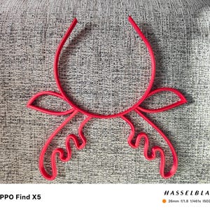 Puede incluir: Un objeto decorativo abstracto de color rojo brillante, con una parte superior curvada y formas estilizadas y fluidas. El objeto est&aacute; centrado en una superficie gris texturizada. El texto "OPPO Find X5" est&aacute; en la parte inferior izquierda.