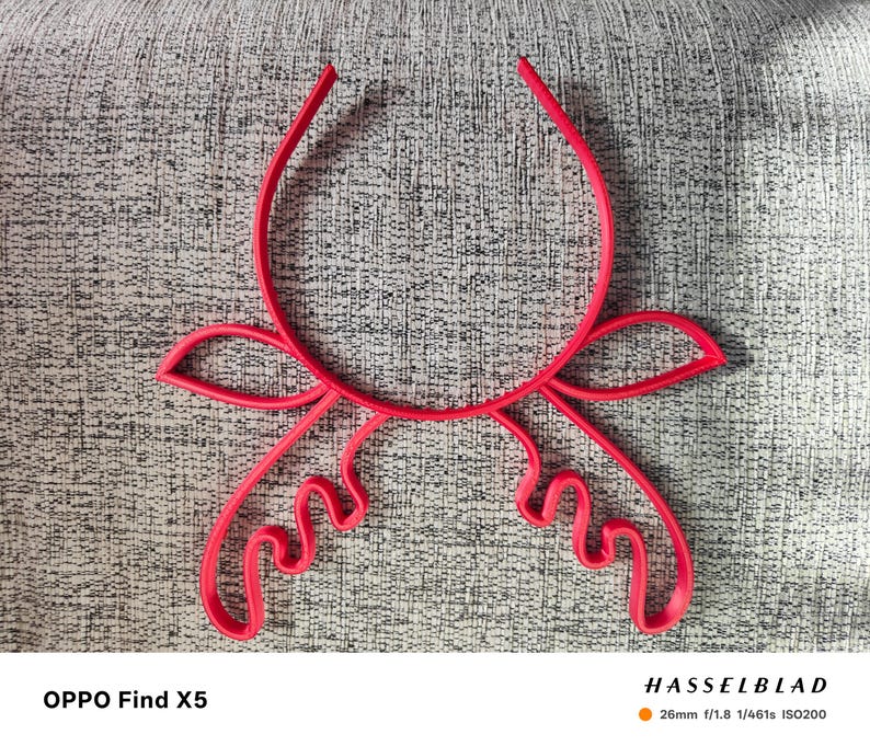 Puede incluir: Un objeto decorativo abstracto de color rojo brillante, con una parte superior curvada y formas estilizadas y fluidas. El objeto est&aacute; centrado en una superficie gris texturizada. El texto "OPPO Find X5" est&aacute; en la parte inferior izquierda.