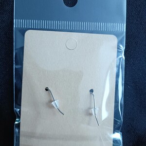 May include: A pair of earrings on a cardboard backing, packaged in a clear plastic bag. The earrings have silver-colored hooks and clear rubber stoppers. The cardboard is a light brown color.