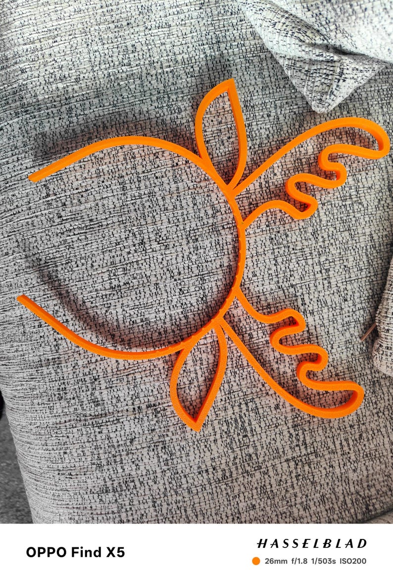 Puede incluir: Dise&ntilde;o floral abstracto de color naranja brillante. Se ve el contorno de una flor o un sol. El objeto est&aacute; hecho de un material s&oacute;lido y se encuentra sobre una superficie gris texturizada. La imagen est&aacute; bien iluminada.