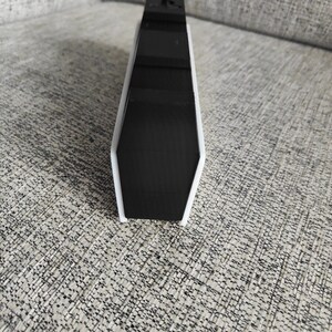 以下が含まれることがあります： 白枠の付いた黒と白の長方形のデバイスが、テクスチャ加工された表面に置かれています。デバイスは洗練されたモダンなデザインです。「OPPO Find X5」の文字が左下に表示されています。