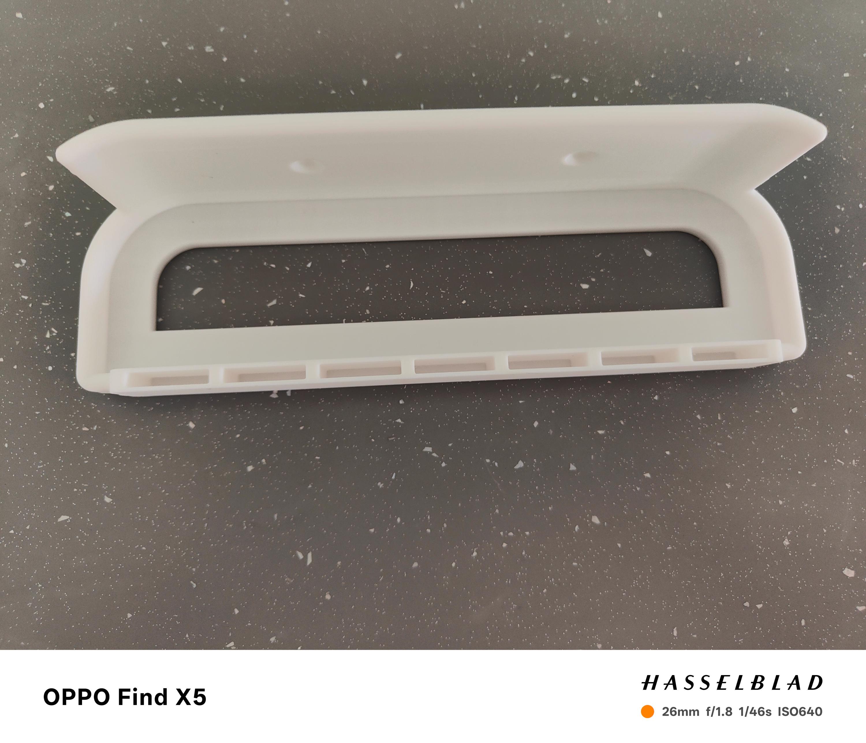 May include: A white, wall-mounted shelf with a curved handle design. The shelf has a rectangular opening and a series of small rectangular slots along the bottom edge. Two holes are visible near the top for mounting.