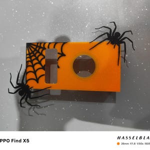 May include: An orange Halloween-themed decoration with a spider web and two black spiders. The decoration has a circular opening and a rectangular shape. The text "OPPO Find X5" is at the bottom.