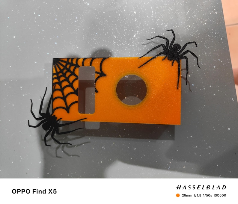 May include: An orange Halloween-themed decoration with a spider web and two black spiders. The decoration has a circular opening and a rectangular shape. The text "OPPO Find X5" is at the bottom.