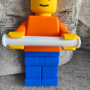 May include: A large, colorful Lego-style figure with a yellow head, orange torso, blue legs, and yellow hands holding a white cylinder. The figure has a smiling face. The image was taken with an OPPO Find X5 camera.