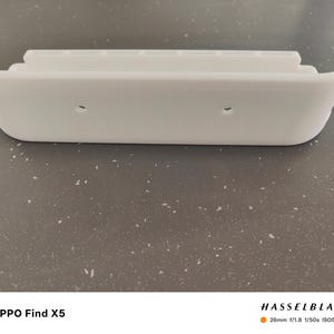 May include: A white, curved, plastic object with a stepped design on top and two small holes. The object has a smooth, clean appearance and a rounded shape. The overall design is minimalist and modern.