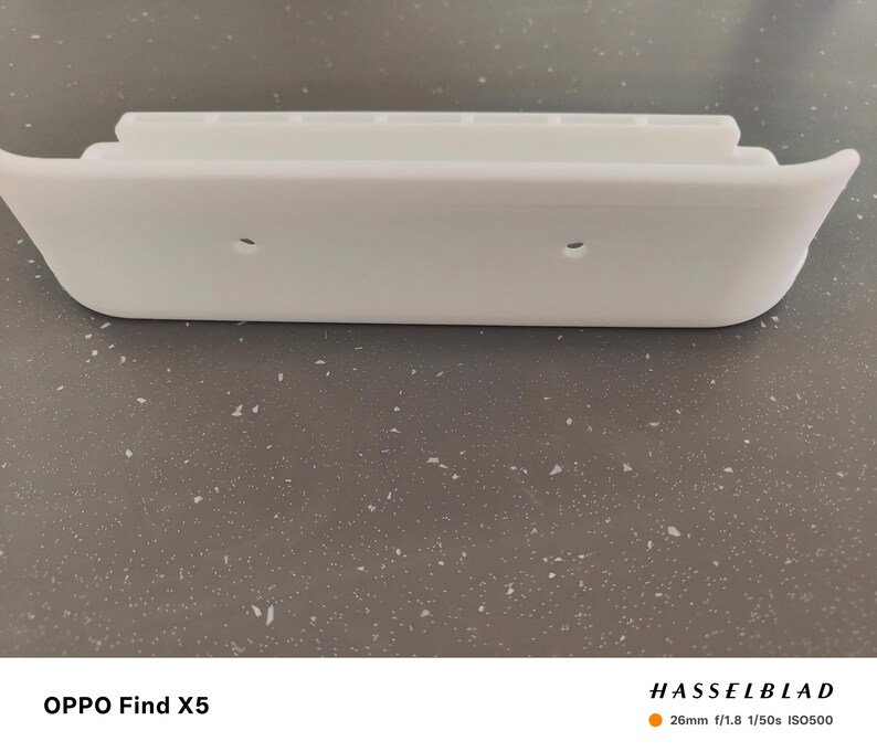 May include: A white, curved, plastic object with a stepped design on top and two small holes. The object has a smooth, clean appearance and a rounded shape. The overall design is minimalist and modern.