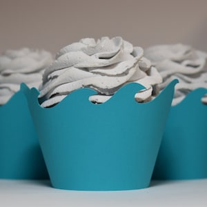 May include: Three white frosted cupcakes with blue wave cupcake liners. The cupcakes are arranged in a row.