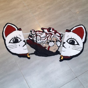 Könnte beinhalten: Ein weißer Teppich mit zwei Katzenköpfen auf jeder Seite und einer Comicfigur in der Mitte. Die Katzenköpfe haben rote Ohren und schwarze Augen. Die Comicfigur hat rot-weißes Haar, eine schwarze Brille und ein schwarz-rotes Outfit.