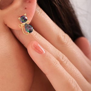 Puede incluir: Pendientes de botón de oro en forma de gato con piedras preciosas azules y verdes iridiscentes.