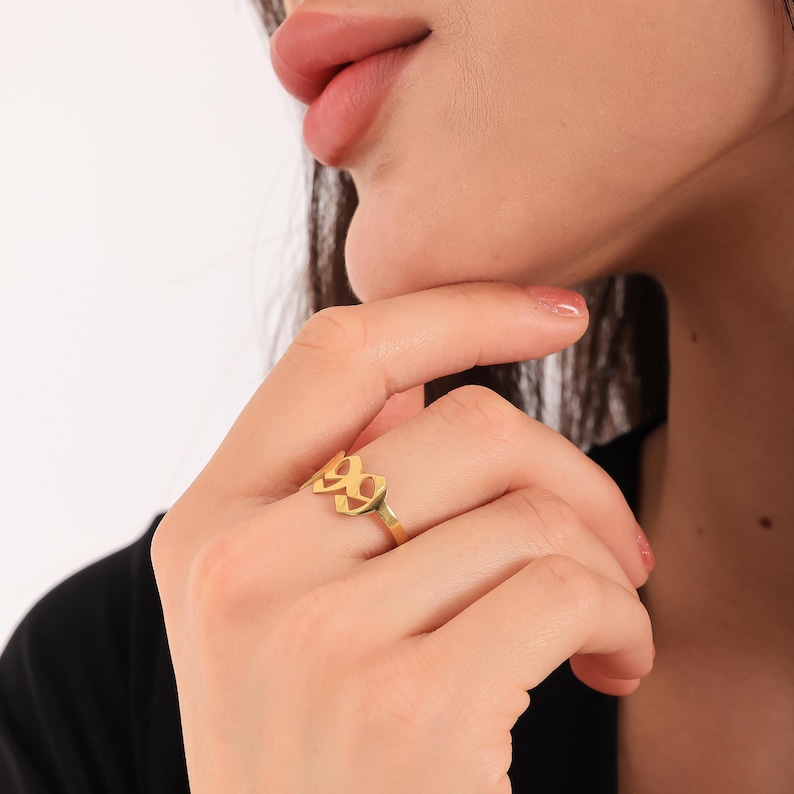 Puede incluir: Anillo de oro con un dise&ntilde;o recortado del n&uacute;mero 99. El anillo se lleva en un dedo.