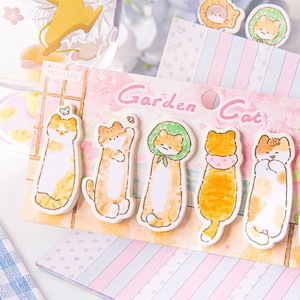 May include: A collection of cat-themed stickers with the words "Garden Cat" printed on the packaging. The stickers feature various cartoon cats in different poses and outfits, with a soft, pastel color palette.