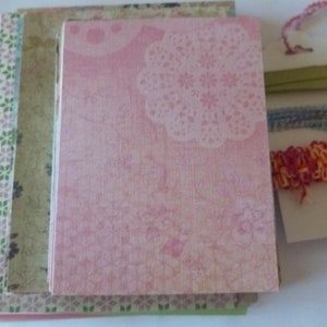 May include: A stack of patterned paper sheets in pink, green, and white. The top sheet has a pink background with a white floral design. The other sheets have a variety of patterns, including floral, geometric, and abstract.