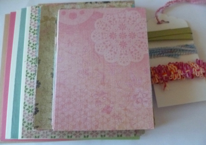 May include: A stack of patterned paper sheets in pink, green, and white. The top sheet has a pink background with a white floral design. The other sheets have a variety of patterns, including floral, geometric, and abstract.