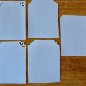 May include: Five blank white card tags with different decorative edges. The tags are on a wooden surface.