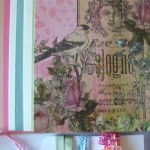 May include: A pink and white patterned paper with a bird, flowers, and the text "Superior" and "E.W. Blogg" on it. There are also several strips of paper in different colors, including pink, blue, and green, and ribbons in green, blue, and pink.