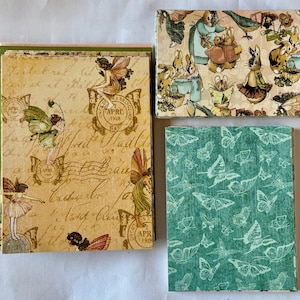 May include: Three decorative boxes with vintage-style designs. One box features fairies and script, another has rabbits and birds, and the third has a teal butterfly pattern. The boxes are likely for storing small items.