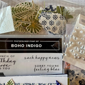 May include: A collection of craft supplies including a stamp set labeled "BOHO INDIGO", floral die cuts, clear epoxy embellishments, and stamps with phrases like "birthday love" and "such happy news".
