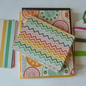 May include: A collection of patterned paper goods, including notebooks and cards. The notebooks feature a colorful chevron pattern, while the cards display a retro telephone dial design. A tag with colorful threads and ribbons is also included.