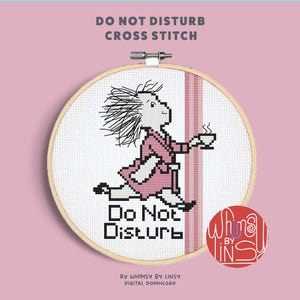 May include: Cross-stitch hoop with a design of a person in a pink robe carrying a cup, with the words "Do Not Disturb" in black. The text "DO NOT DISTURB CROSS STITCH" is at the top. A red circle with text is on the bottom right.