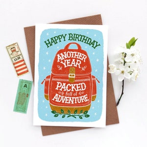 May include: A blue and white birthday card with a red backpack illustration. The text on the card reads "Happy Birthday Another Year Packed Full of Adventure".