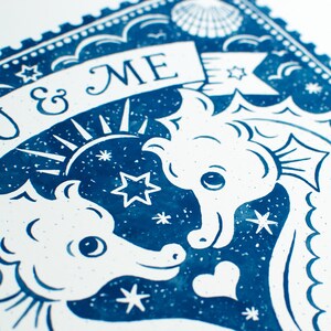 K&ouml;nnte beinhalten: Eine blaue und wei&szlig;e Illustration von zwei Seepferdchen, die sich gegen&uuml;berstehen, mit einem Banner, auf dem "You & Me" steht. Der Hintergrund ist ein blauer Sternenhimmel mit einer wei&szlig;en Muschel in der oberen Ecke.