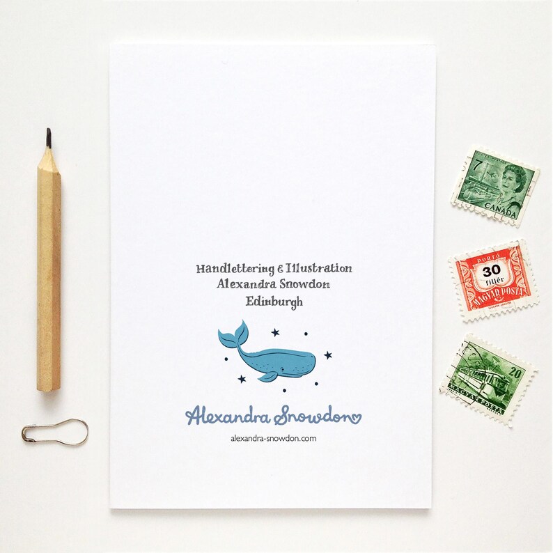 May include: A white card featuring a blue whale illustration and the text "Alexandra Snowdon". A pencil, paperclip, and postage stamps are placed beside the card. The card also has the text "Handlettering & Illustration Alexandra Snowdon Edinburgh".