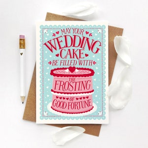 May include: A wedding card with a pink and white cake illustration. The card reads "May your wedding cake be filled with the frosting of good fortune".