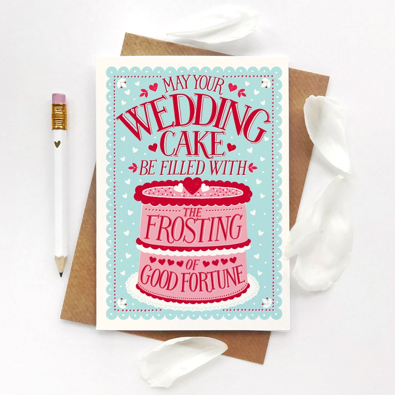 May include: A wedding card with a pink and white cake illustration. The card reads "May your wedding cake be filled with the frosting of good fortune".