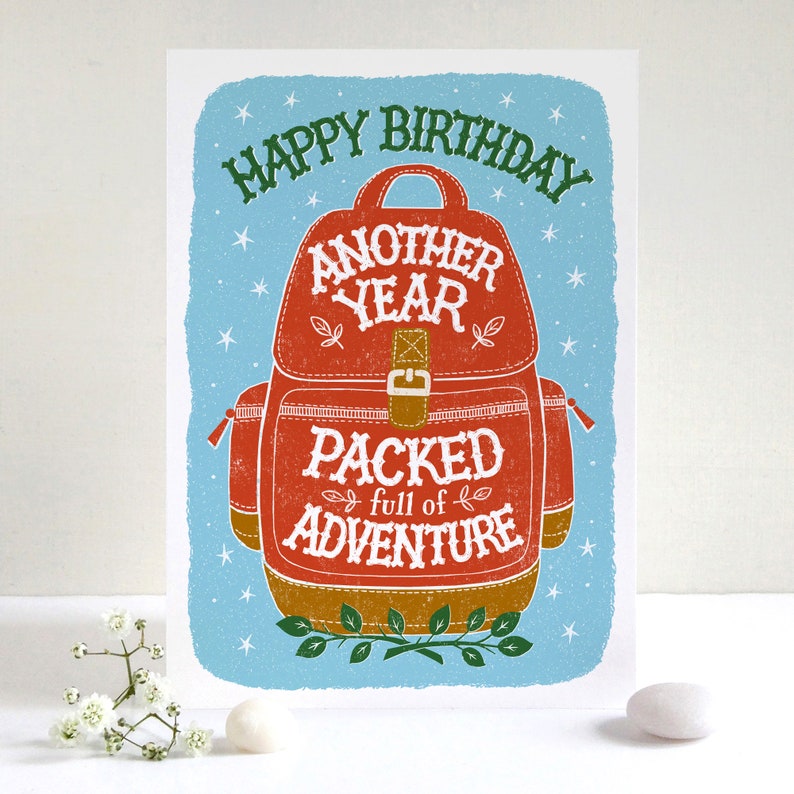 May include: A red and brown illustrated birthday card with a backpack and the text "Happy Birthday Another Year Packed full of Adventure".