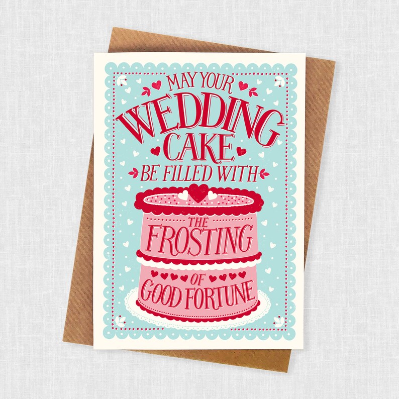 May include: A light blue card with a white border and a pink and red wedding cake illustration. The text reads "May your wedding cake be filled with the frosting of good fortune."