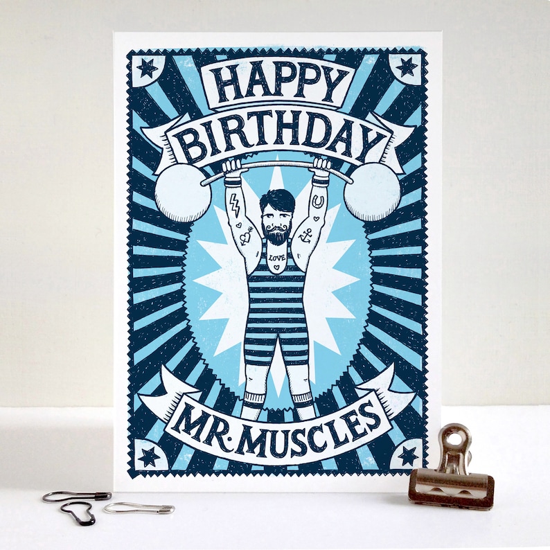 Pu&ograve; includere: Un biglietto d'auguri illustrato in blu e bianco con un uomo forte dei cartoni animati che solleva pesi. Il biglietto dice "Buon compleanno Mr. Muscles".
