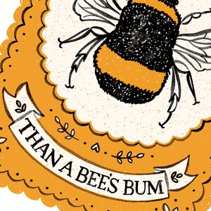 May include: A yellow and black bee with wings and legs is illustrated on a yellow background with a white border. The text "THAN A BEE'S BUM" is written on a white ribbon.